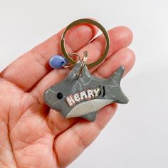 a hand holding a metal keychain with a shark on it