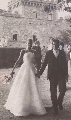 black and white photograph of a bride and groom walking towards an old castle with people in the background