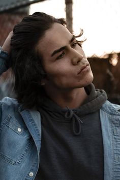 a young man with long hair wearing a denim jacket and looking off to the side