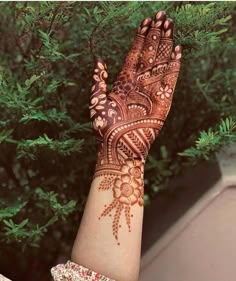 a woman's hand with henna on it and green trees in the background