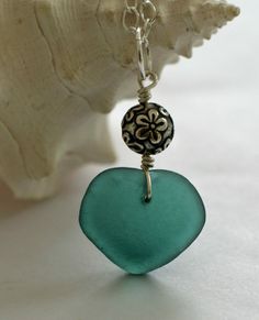 a green heart shaped glass pendant on a silver chain with a flower charm hanging from it's end