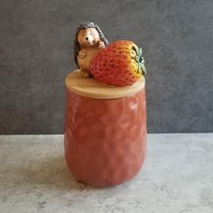 a ceramic hedge sitting on top of a strawberry jar with a small hedge figurine next to it