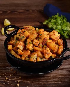 a black bowl filled with fried food on top of a wooden table next to lemon wedges