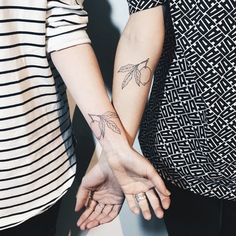 two people holding hands with tattoos on their arms