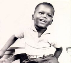 a black and white photo of a young boy sitting on a stool smiling at the camera