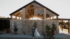 a bride and groom standing in front of a brick building with large windows at sunset