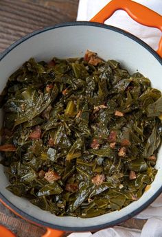 a white bowl filled with collard greens on top of a wooden table next to an orange handled utensil