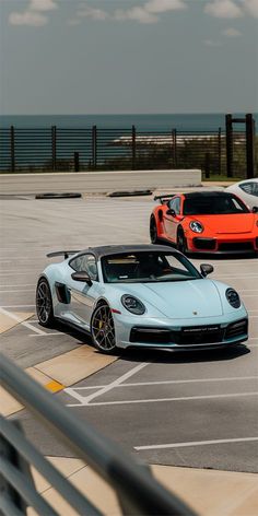 three different colored sports cars parked in a parking lot next to each other with the ocean in the background