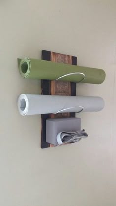 three different colored yoga mats are hanging on the wall next to a person's hand