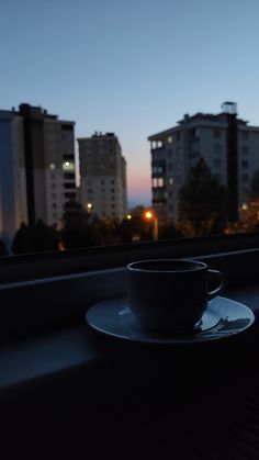 a cup and saucer sitting on a window sill in front of some buildings