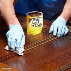 a man in blue gloves is holding a can of gel stain on a wooden table