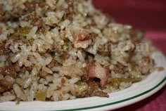 a white plate topped with rice covered in meat and veggies next to a red table cloth