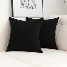 two black pillows sitting on top of a white couch next to a framed photo and plant