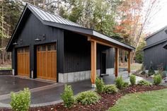 two black garages with wooden doors in front of trees and grass on the ground