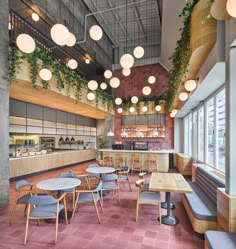 an empty restaurant with tables and chairs in front of large windows, potted plants hanging from the ceiling