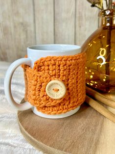 an orange crocheted coffee cup cozys next to a brown vase