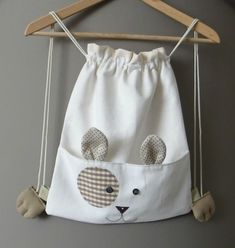 a white bag with a bear face on it hanging from a wooden hanger next to a gray wall