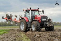 a tractor is plowing the land in front of some other farm animals on a cloudy day