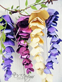 purple and yellow flowers are hanging from a branch with green leaves on the top, along with white wood planks