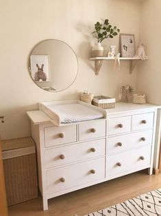 a white dresser sitting in a bedroom next to a mirror and shelf with pictures on it