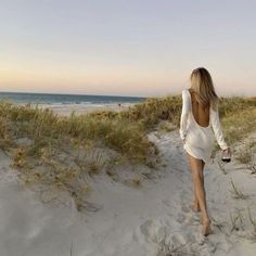 a woman walking down a sandy beach next to the ocean