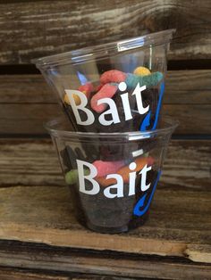 two plastic cups filled with different colored candies on top of a wooden table next to each other