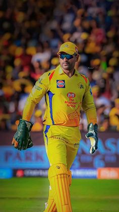 a man in yellow uniform walking across a field with his hand on his hip and wearing green gloves