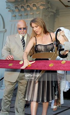 a man and woman cutting a red ribbon at an event with other people in the background