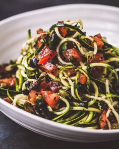 a white bowl filled with zucchini noodles and tomatoes on top of a table