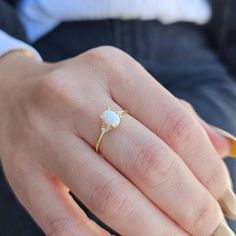 a close up of a person's hand wearing a ring with a white opal