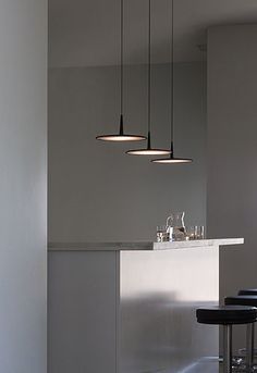 three lights hanging over a bar with wine glasses on the counter and two stools