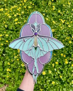 a hand holding up a stained glass flower in front of some yellow and green flowers