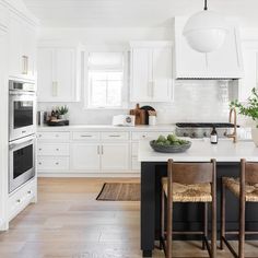 a kitchen with white cabinets and black island in the center is surrounded by wooden chairs