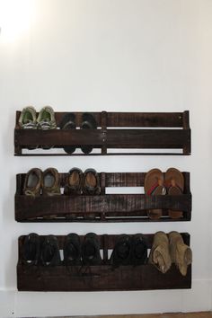 three wooden shelves holding pairs of shoes and slippers on top of each other in front of a white wall