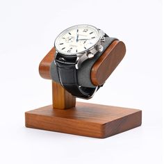 a watch sitting on top of a wooden stand with a black leather strap around it