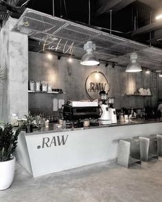 the interior of a raw restaurant with concrete walls and exposed ceilings, plants in pots on either side of the counter