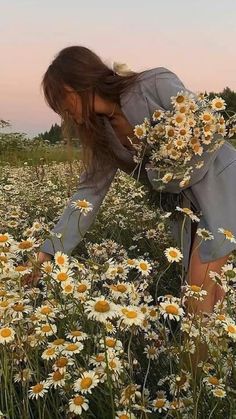 a woman kneeling down in a field of daisies