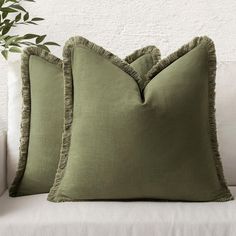 two green pillows sitting on top of a white couch next to a potted plant