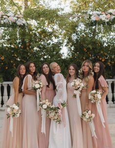 a group of women standing next to each other wearing dresses and holding bouquets in their hands