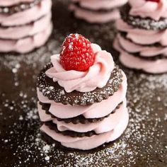 some cookies with pink frosting and a strawberry on top are stacked up next to each other