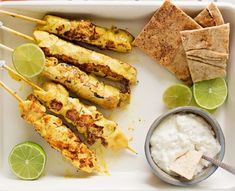 chicken skewers with pita chips, sour cream and lime wedges on a tray