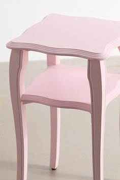 a small pink table with two chairs on it's legs and one chair up against the wall