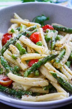 pasta with asparagus, tomatoes and pesto in a white bowl on a table