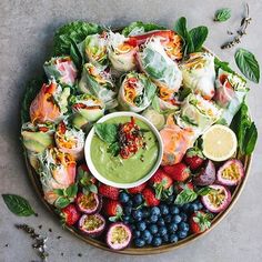 a platter filled with fruit and vegetables on top of a gray table next to a bowl of guacamole