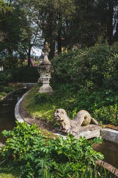 a stone lion statue sitting on top of a lush green hillside next to a river