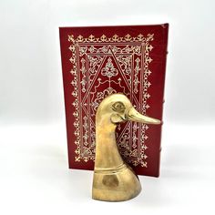 a golden duck statue next to a red book with an intricate design on it's cover