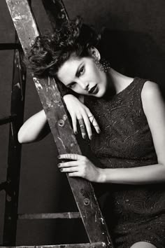 a black and white photo of a woman leaning up against a wooden ladder with her hand on her shoulder