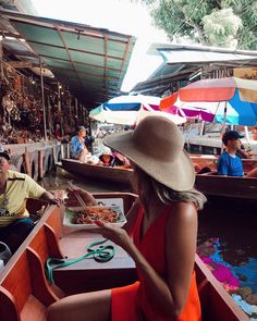 a woman in an orange dress and hat is sitting on a boat with other people