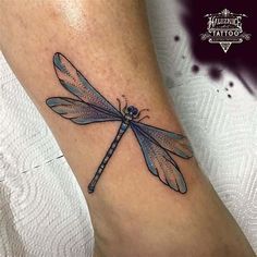 a small dragonfly tattoo on the ankle is shown in black and grey ink with blue eyes