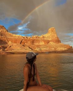 a woman sitting on top of a boat in the water with a rainbow behind her